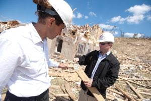 two men wearing hard hats examine a piece of wood in a debris field from the April 27, 2011 tornado