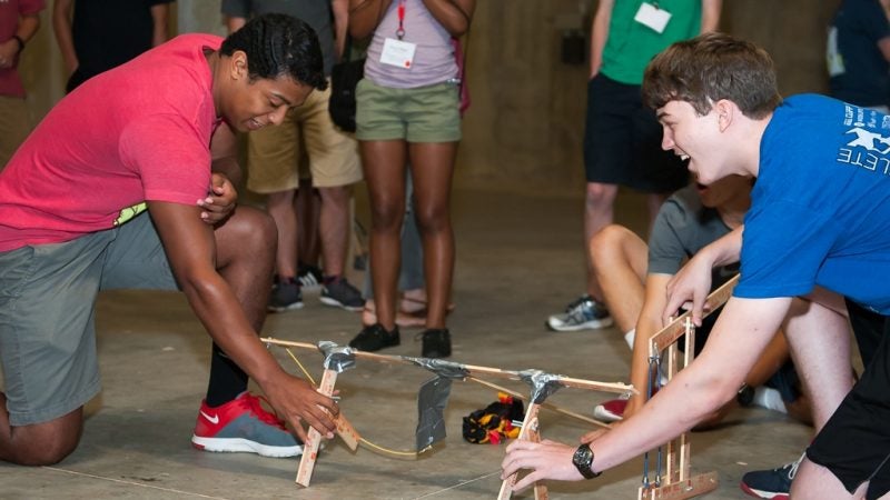 Two students holding a small catapult that was built during a summer camp
