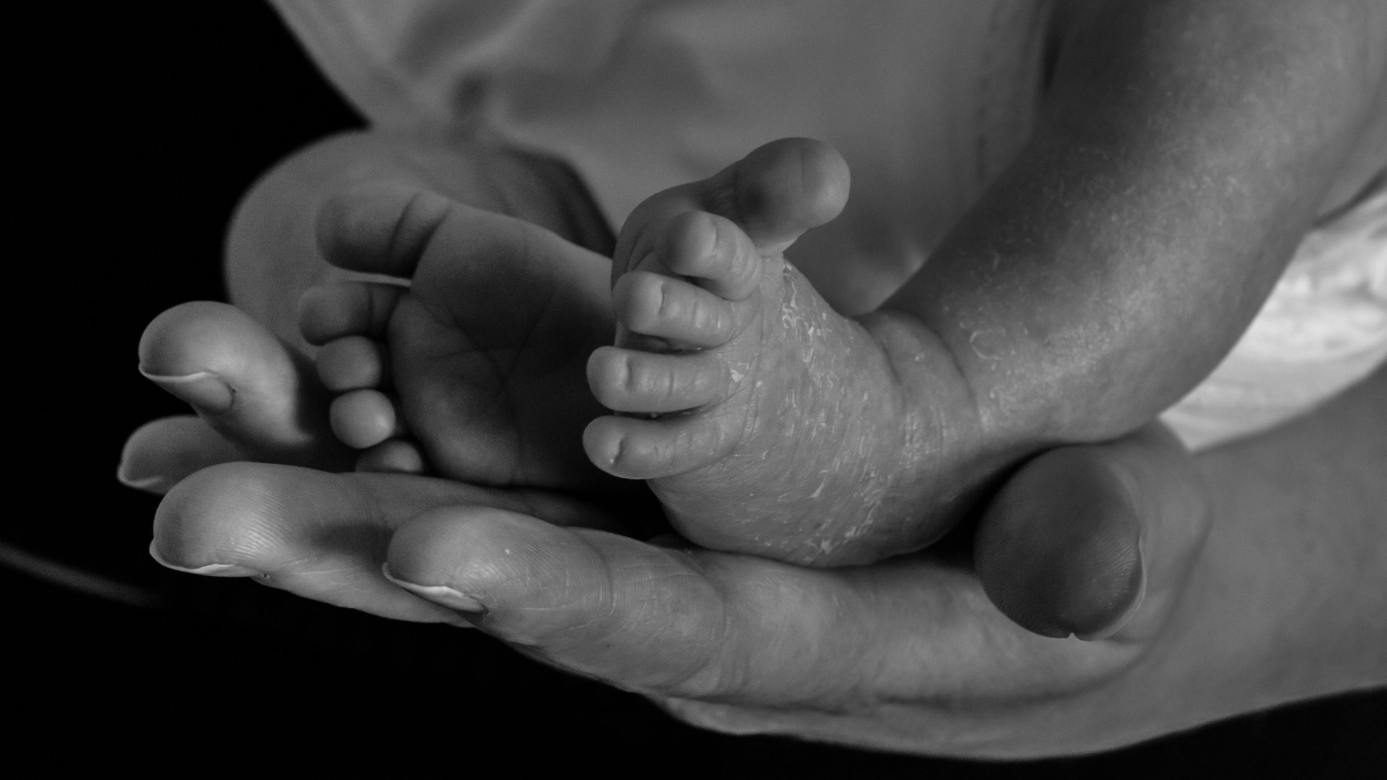 black and white close-up photgraph of an adult holding an infants feet in their hands