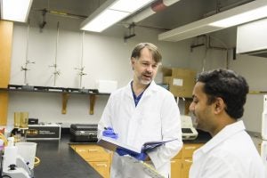 Two scientists in white coats discuss research in a lab.