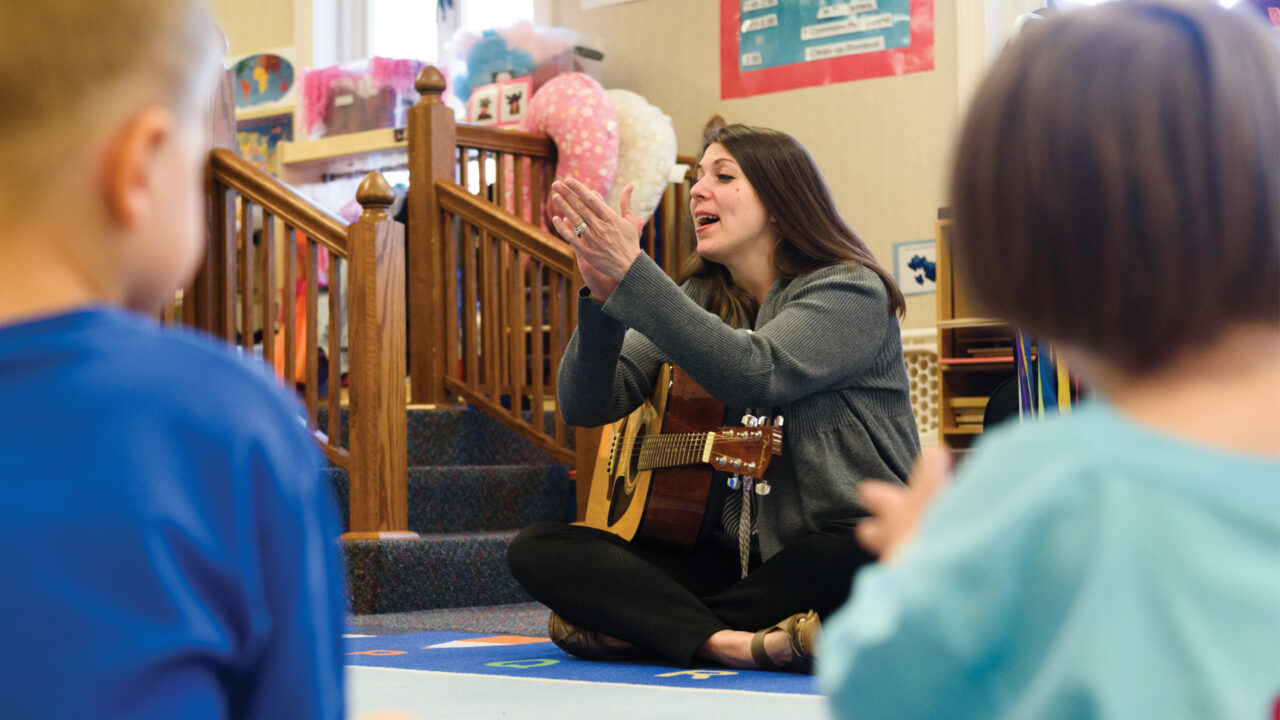 A teacher playing a guitar for students