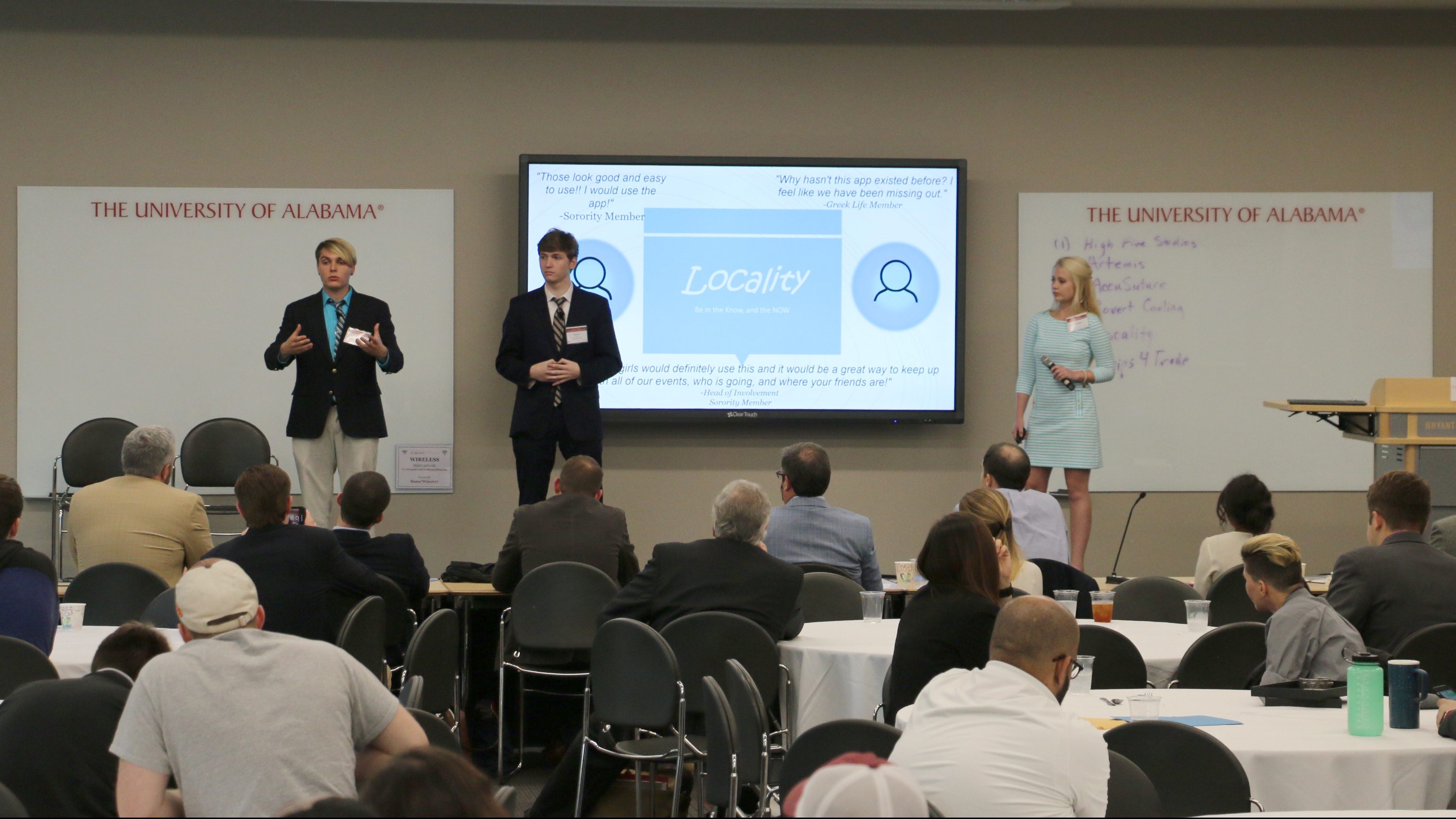 three students give a presentation to a room of people during a pitch competition