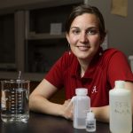 A woman in an Alabama polo shirt poses at a lab desk with containers.