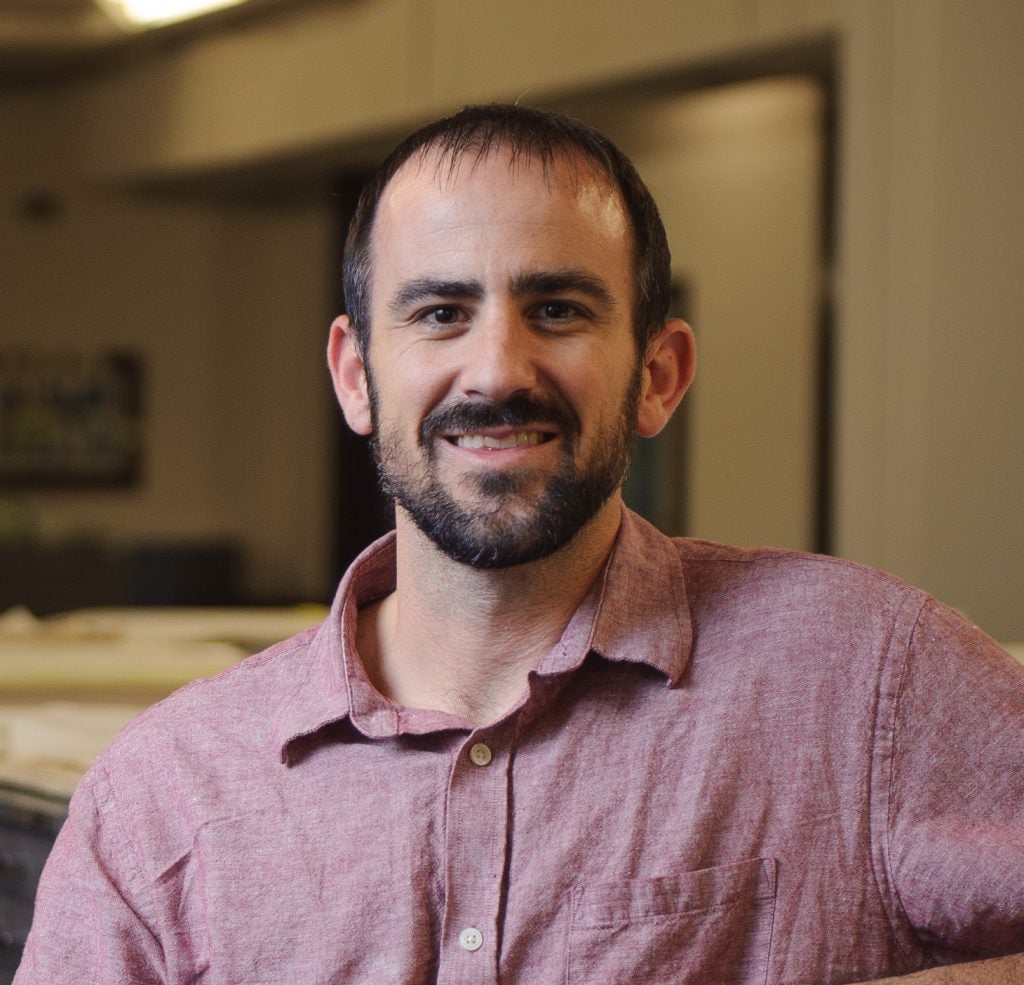 A professor in a button-down shirt poses for a photo in an archival room.