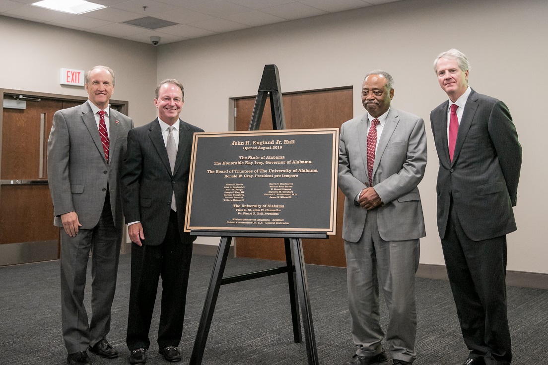 John England stands with UA officials at plaque naming John England Hall points to wall honoring his accomplishments