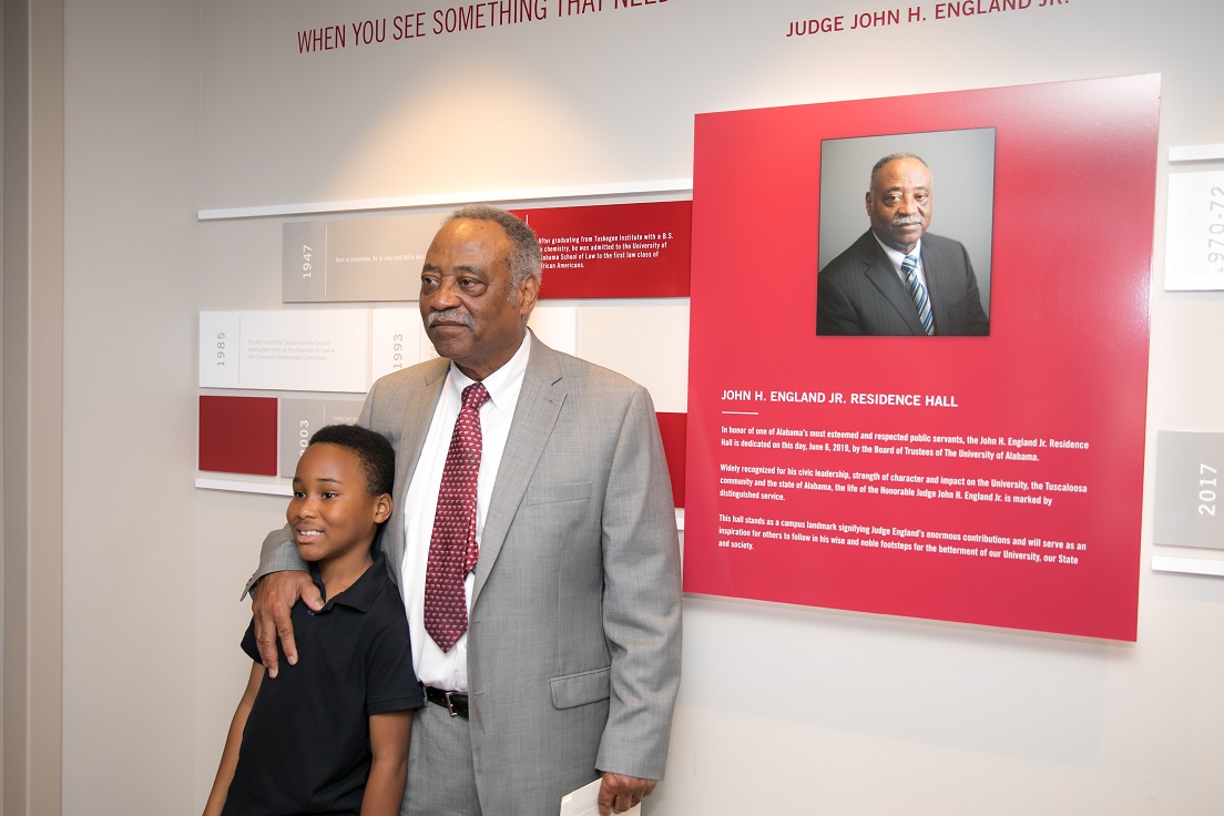 John England standing with child in front of wall honoring his accomplishments
