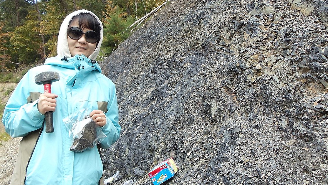 A student collects fossil samples from a shale outcrop.