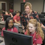 A female college professor works on a computer activity with prospective students