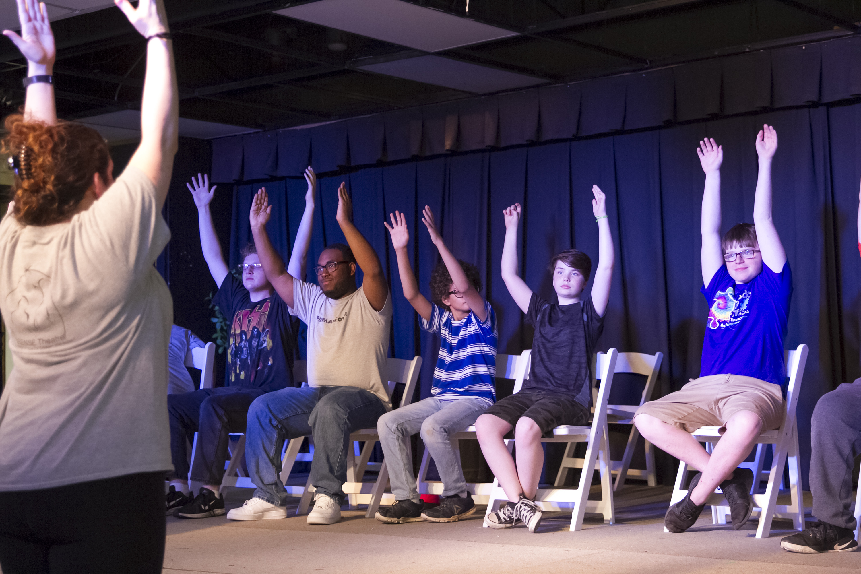 Theatre actors ages 10 to 17 hold their arms in the air as they rehearse a play.