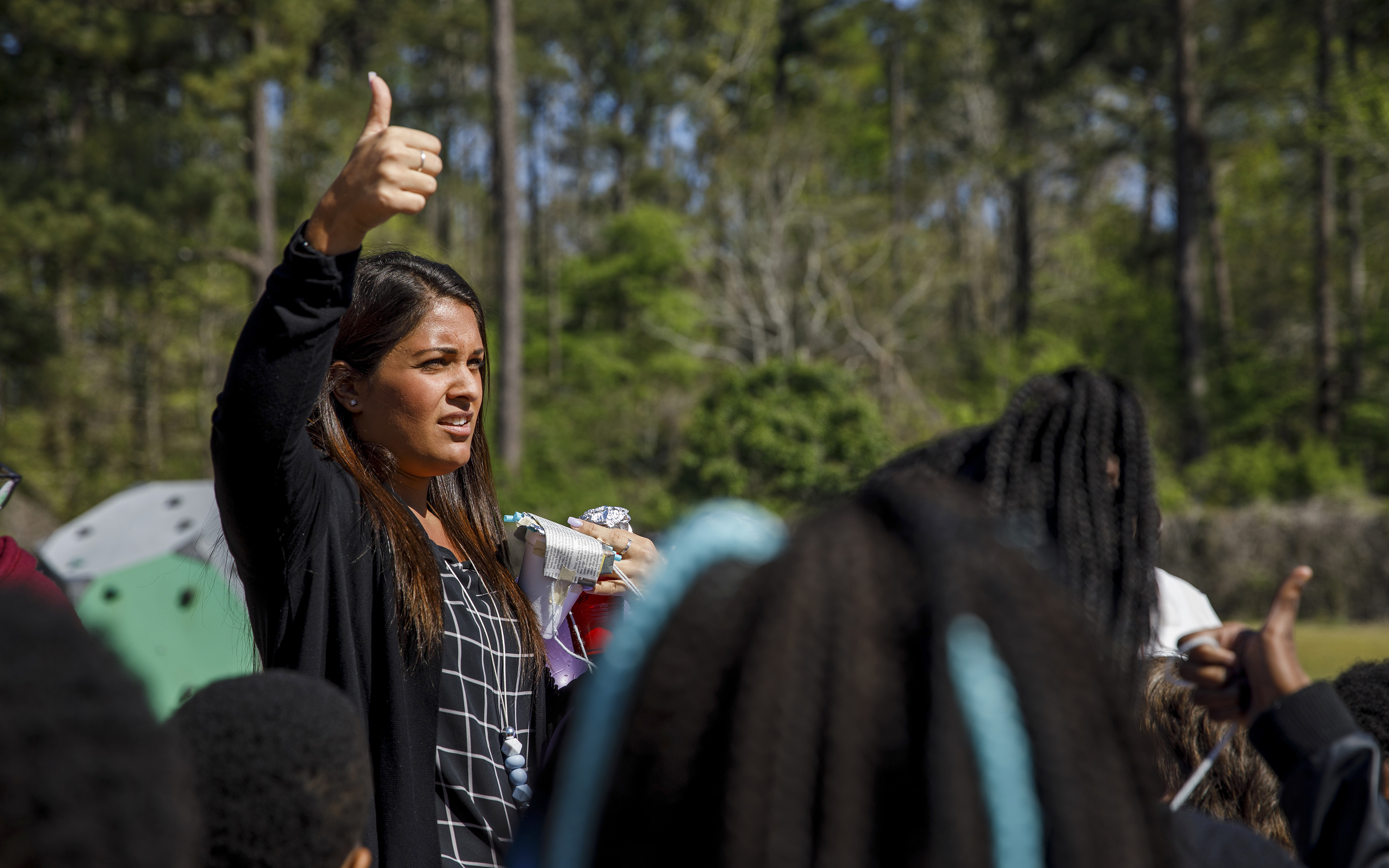 A college student signals thumbs up to elementary students during a group science experiment.