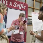 A male university student reviews a photo on a cell phone at orientation