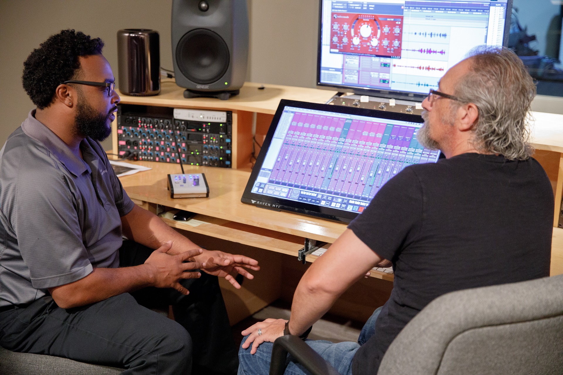 Two men talk while sitting at a table in a campus recording studio.