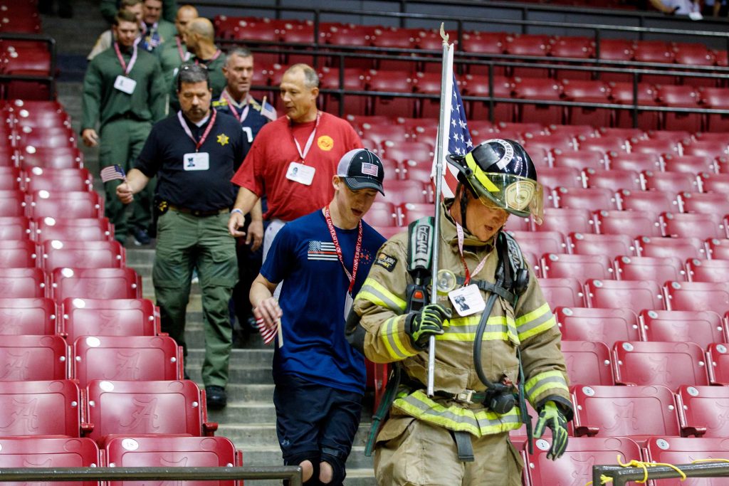 A firefighter carrying a U.S. flag leads a line of first responders as they walk down stairs at Coleman Coliseum