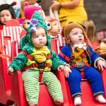 Babies wearing Halloween costumes riding in a stroller together
