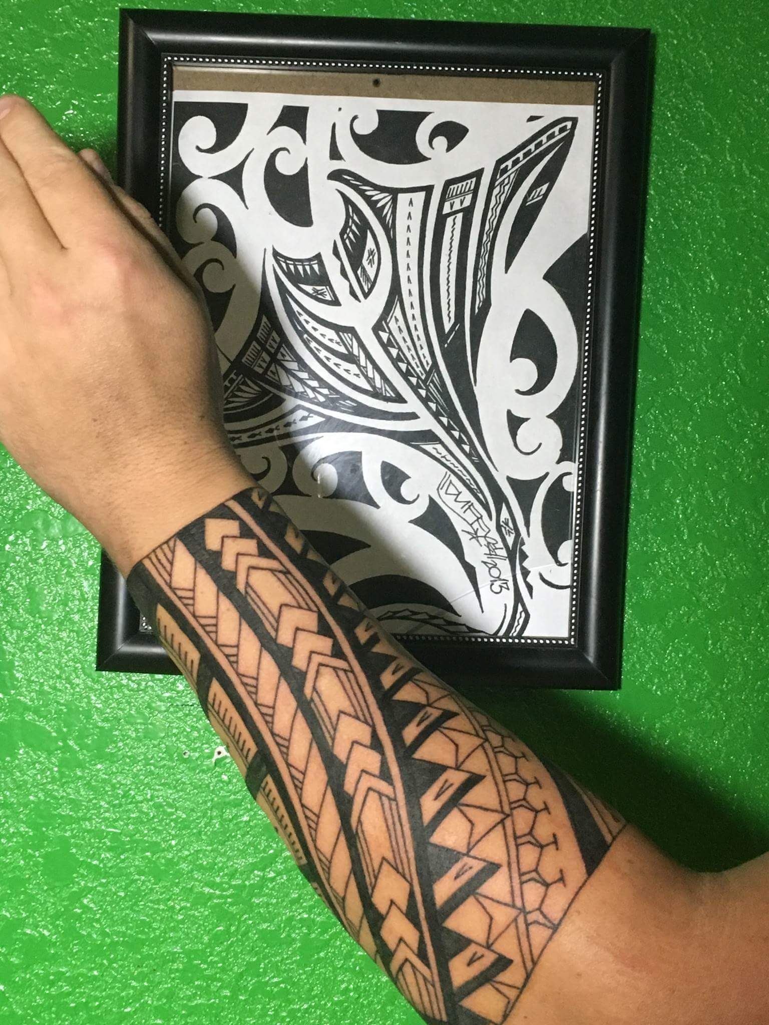 A forearm covered with a tattoo rests on a table on top of a design that inspired the tattoo.