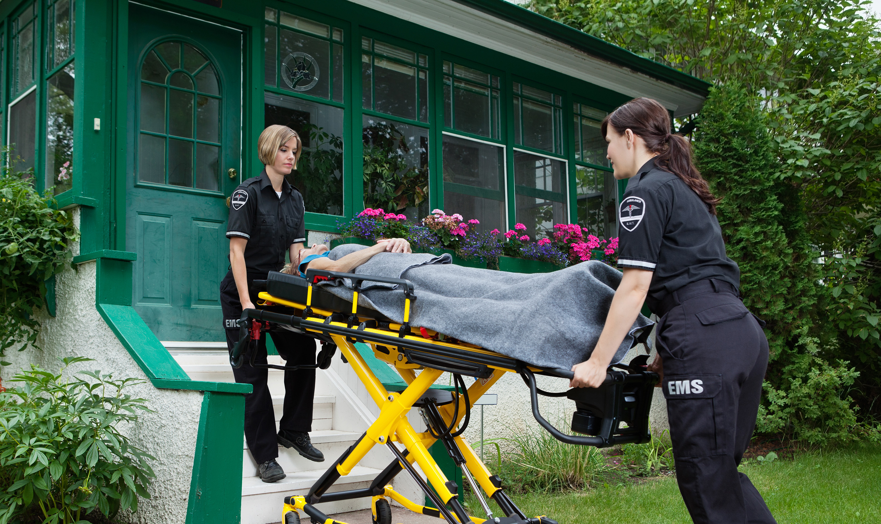 Two female paramedics escort a patient on a stretcher out of a home