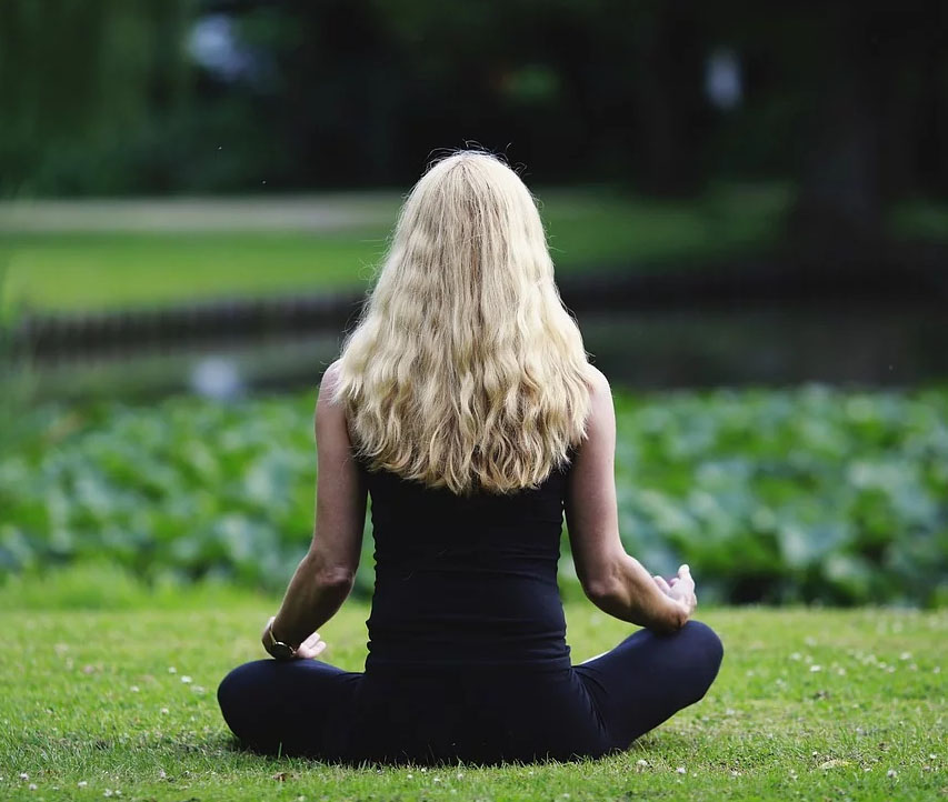 A woman meditating by a pond.