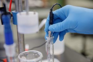 A blue-gloved hand works on a lab bench inserting materials in a beaker.