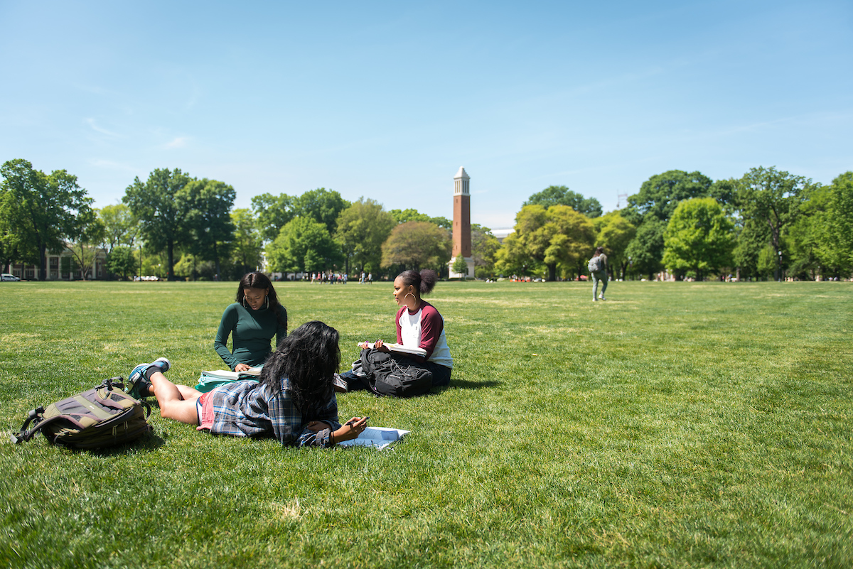Three students study on the Quad. Denny Chimes is in the background.