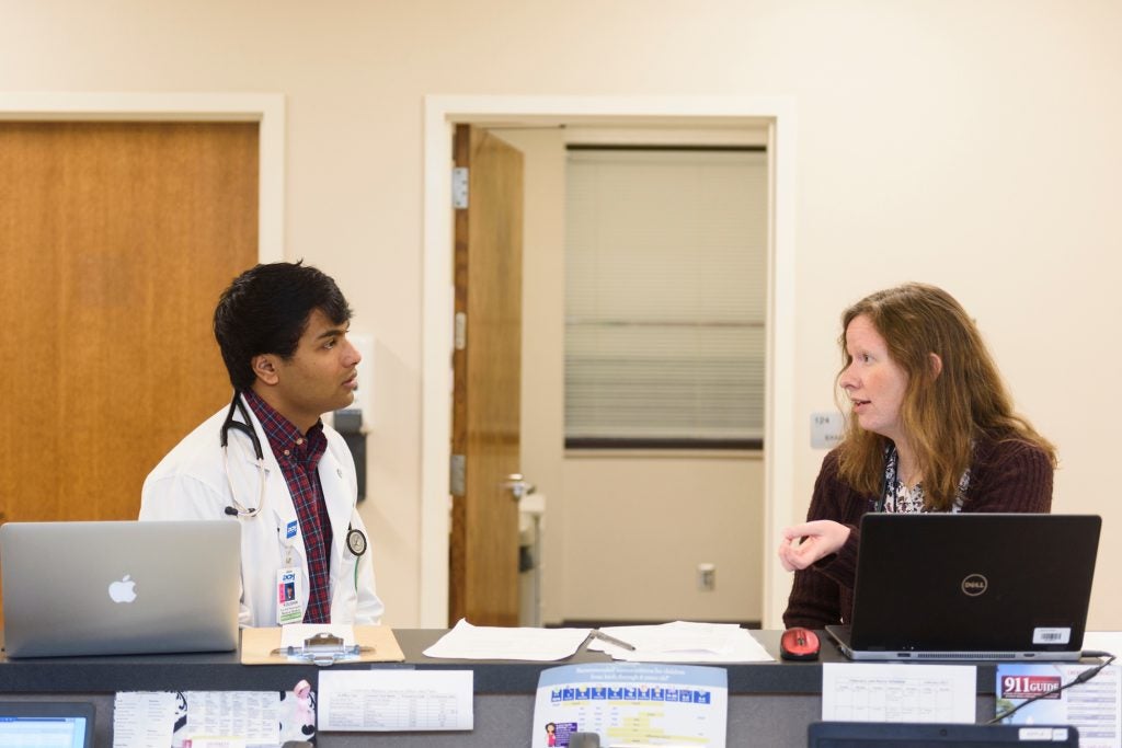 A doctor and colleague talking in a hospital hallway.