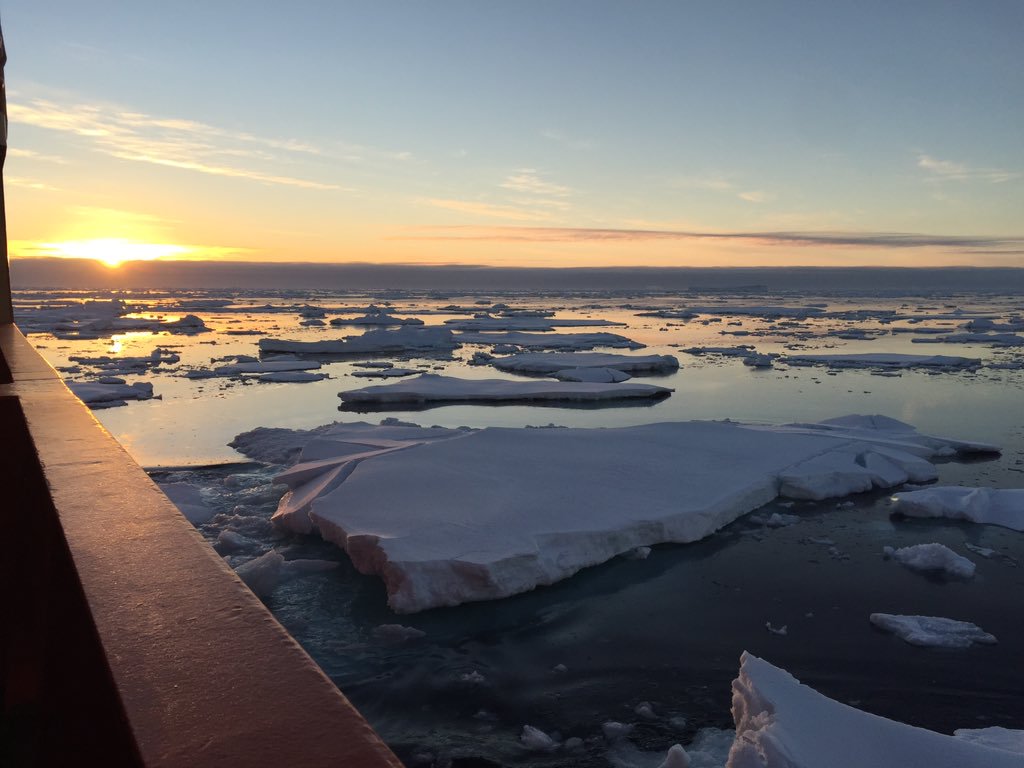 The sun sits on the horizon above the ice-laden sea off the coast of Antarctica.