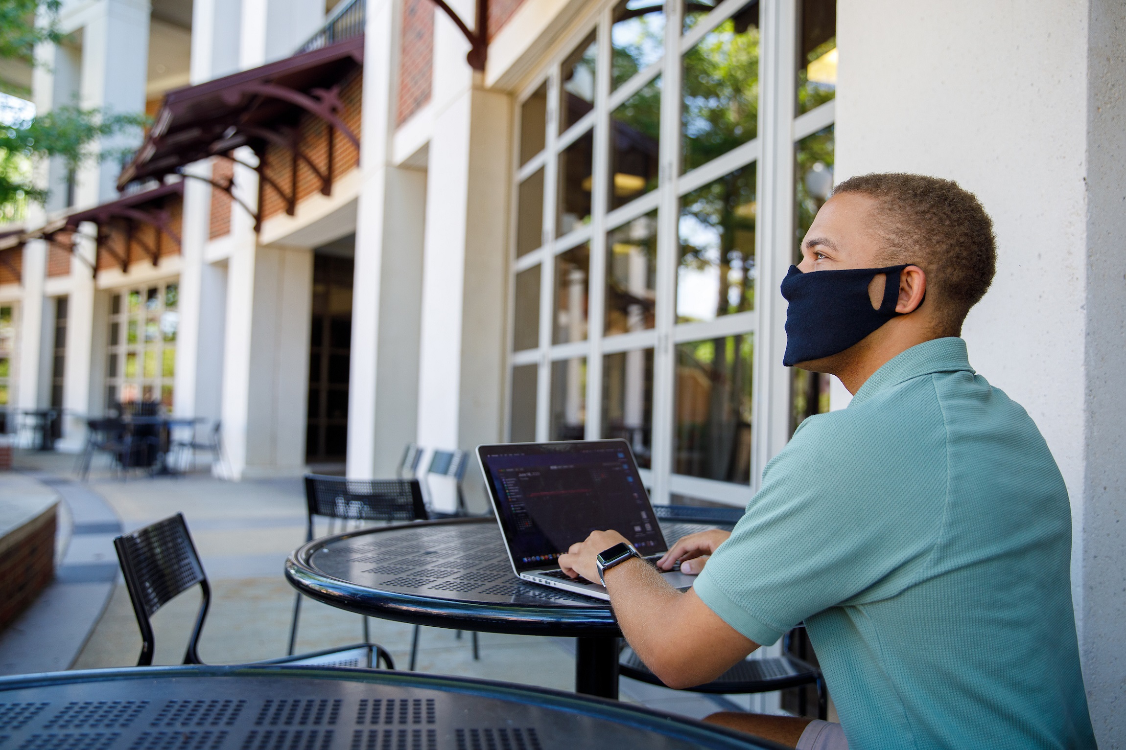 A man uses a laptop in outdoor table wearing a mask.