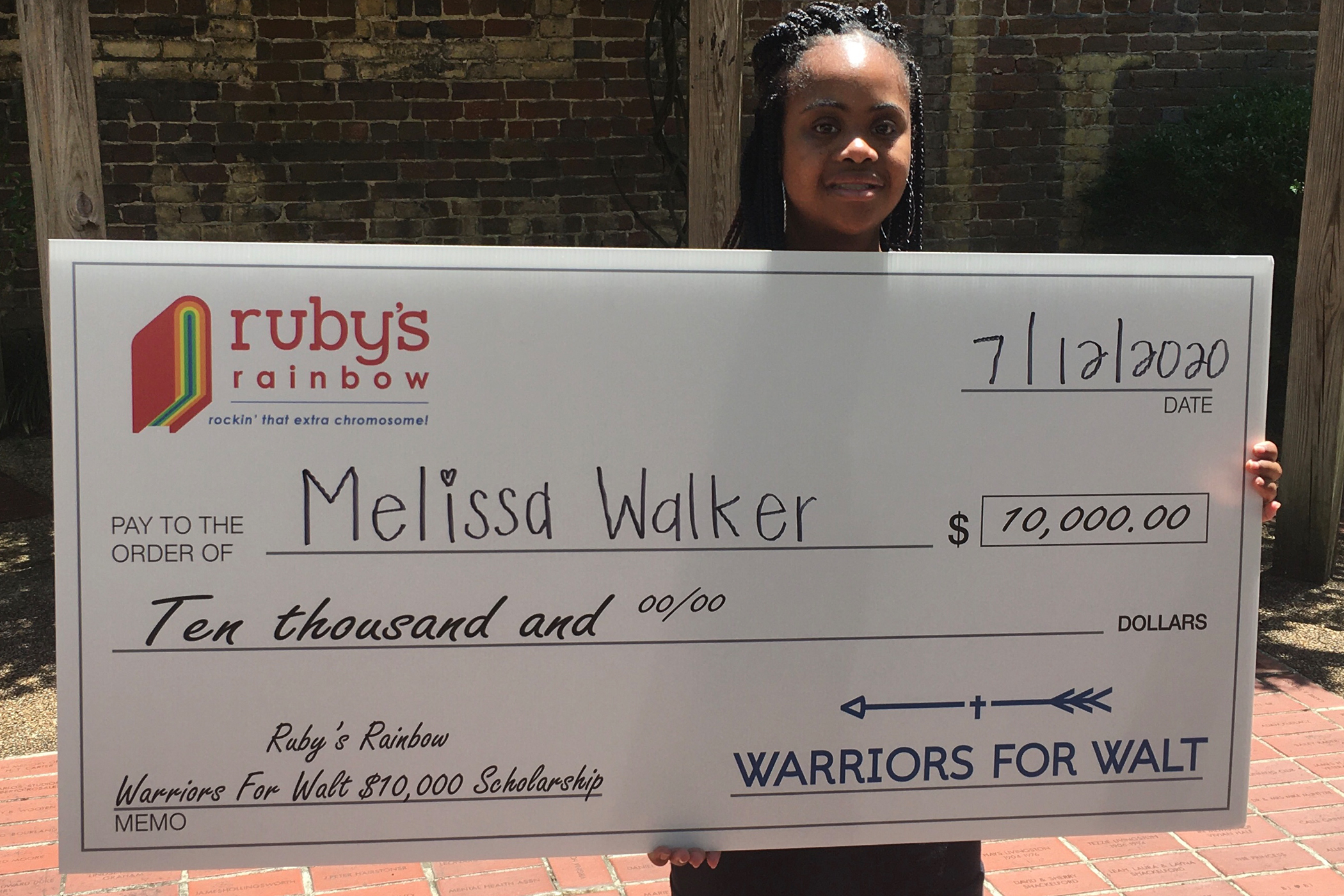 Melissa Walker holding a check representing the Ruby's Rainbow Warriors for Walt Scholarship