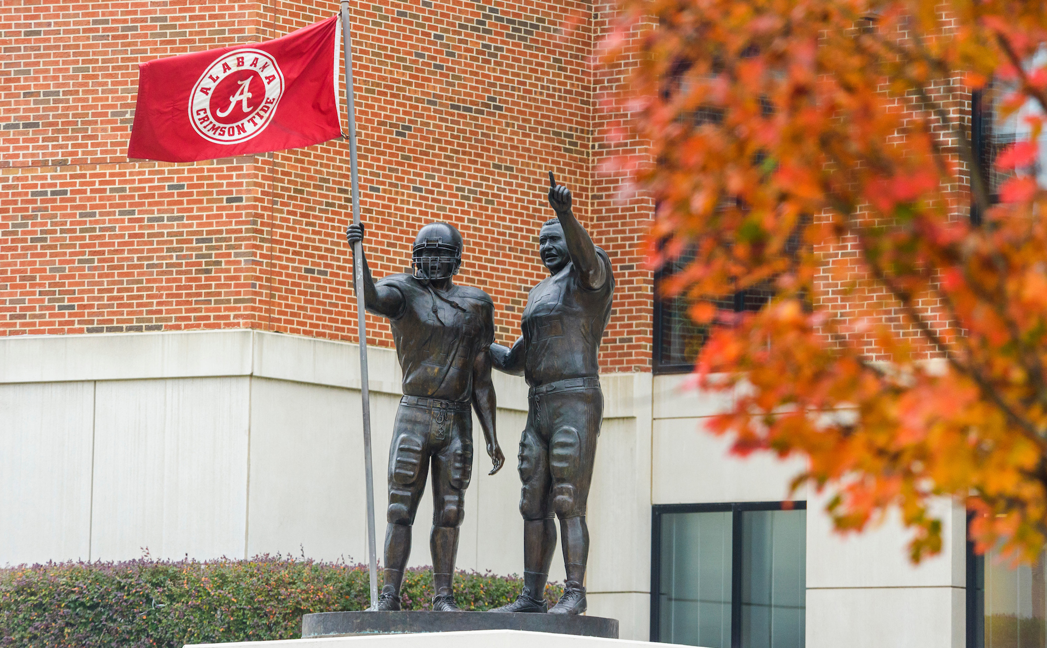 A statue of football players holding an Alabama flag outside of Bryant-Denny Stadium.