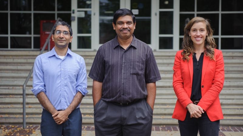 Two men and a woman stand for a photograph in front of a building.