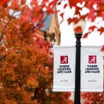 two lampost banners reading "Where legends are made" set against bright-color autumn leaves in the trees