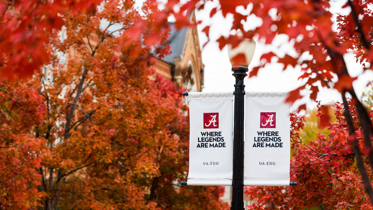two lampost banners reading "Where legends are made" set against bright-color autumn leaves in the trees