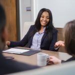 Female student sitting at a conference table talking to other students.