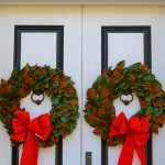 Fresh magnolia wreaths with red bows on white double doors