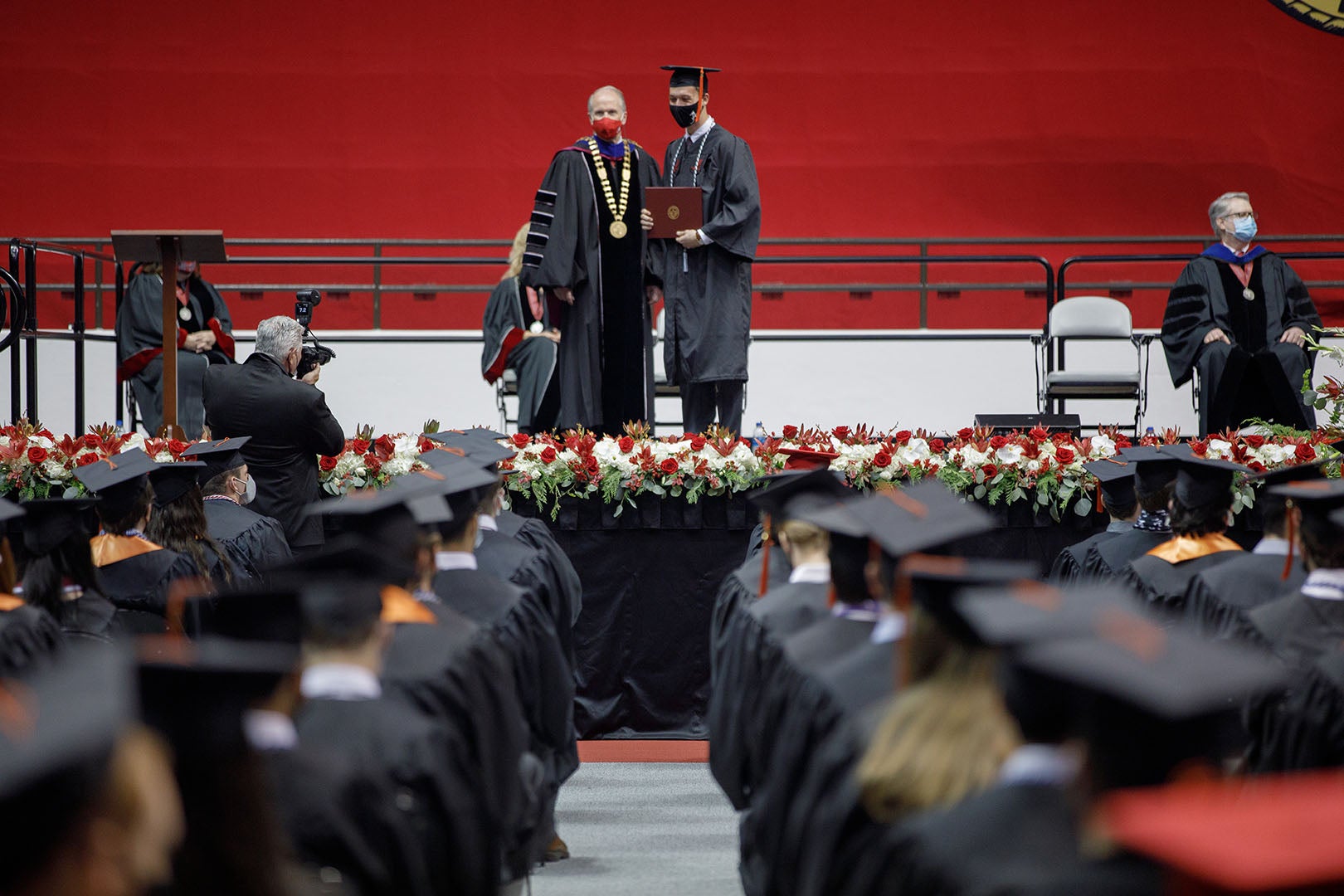 A crowd's view of the commencement stage where President Bell poses with a graduate who just received their degree.