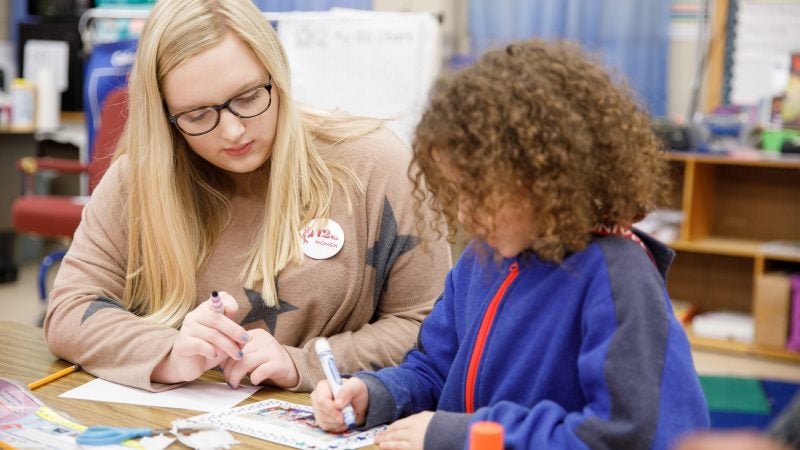 A teacher looking over a young student's shoulder while the student colors.