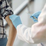 Healthcare provider with gloved hands administors a shot to a patient with rolled up sleeve.