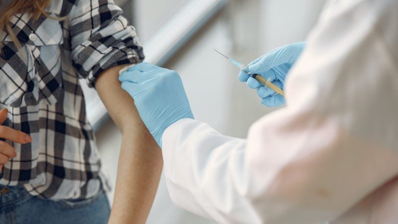 Healthcare provider with gloved hands administors a shot to a patient with rolled up sleeve.