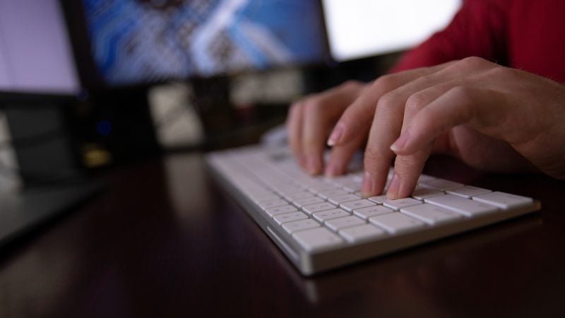 Hands type on a computer keyboard on a desk.