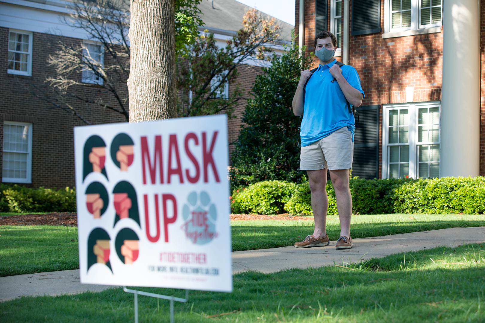 A UA student stands behind a mask sign on campus.