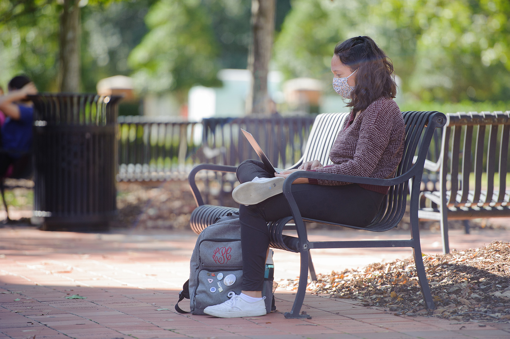 A student sets on a bench working on her computer on the UA campus.