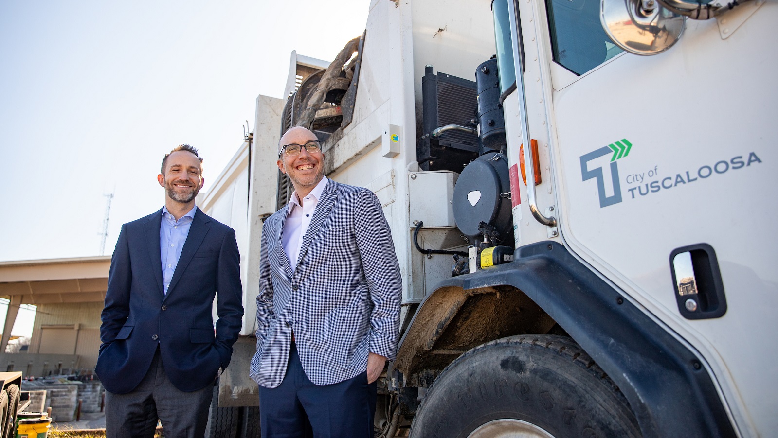 Two men in suits pose in front a Tuscaloosa garbarge truck.