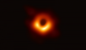 A black hole is seen in the center of a circle of orange and yellow light.