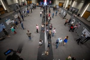 A room of people viewed from above as they examine research poster presentations.