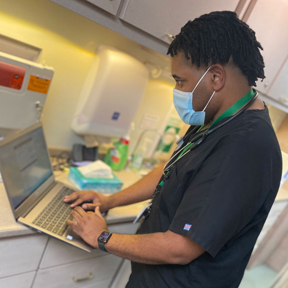 a nurse in scrubs and a face mask types on a laptop in a clinic