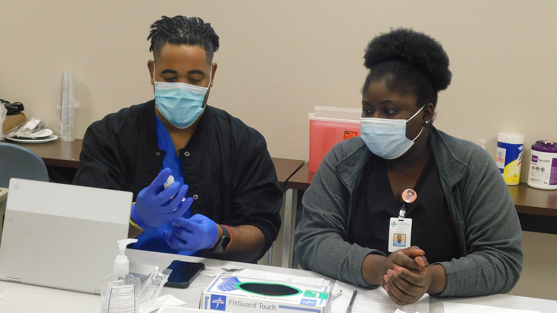 twp nurses in face masks examine a vial while sitting at a table