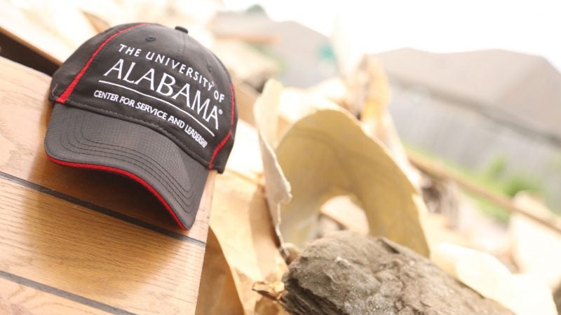 a ball cap hat reading "The University of Alabama Center for Service and Leadership" sits on top of a pile of debris at a volunteer work site.