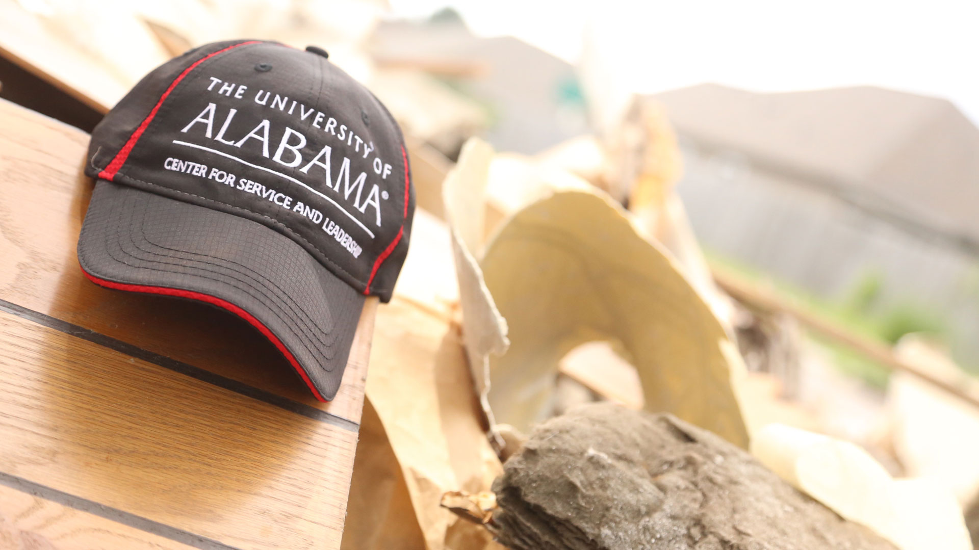 a ball cap hat reading "The University of Alabama Center for Service and Leadership" sits on top of a pile of debris at a volunteer work site.