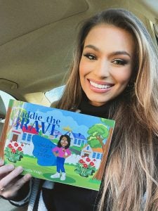 young women holds up a children's book titled "Maddie the Brave"