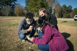 Three people gather around a sensor placed in the ground as part of scientific research.