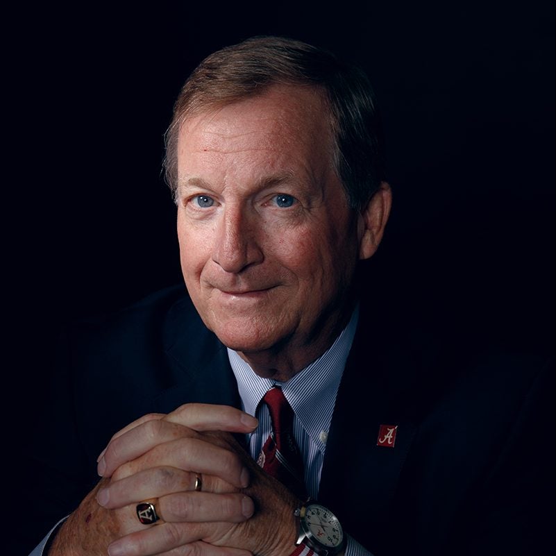 Sitting with his hands crossed, Keith Norton is in a blue blazer with an Alabama A lapel pin and his A-Club ring.